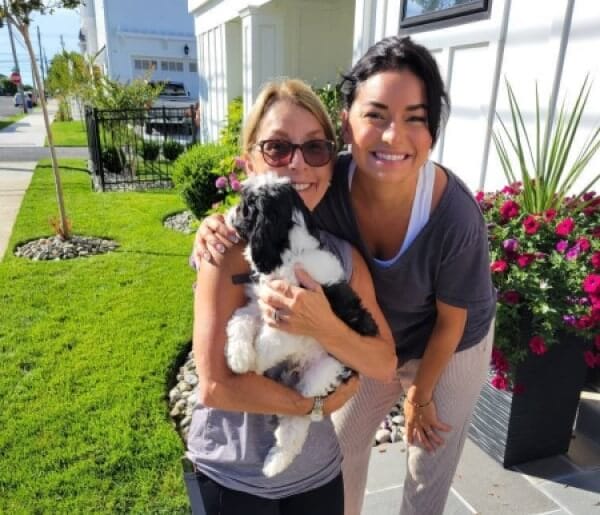 Two women providing pet relocation services in front of a house with their adorable dog.